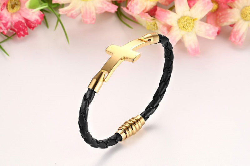 Gold bracelet with black braided cord on a light pink background with flowers.