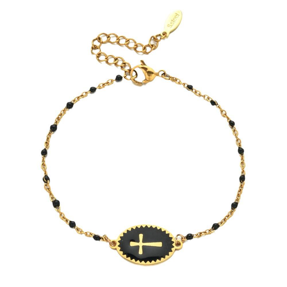 Gold bracelet with black beads and a central black disc featuring a gold cross on a white background.