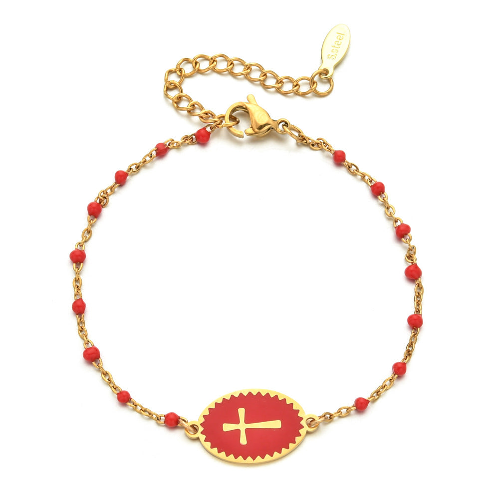 Gold bracelet with red beads and a red disc featuring a gold cross on a white background